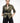 Model wears the asymmetric body piece styled with a linen green shirt and black pants