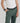 a male model wearing wide black yvy leather bracelet with silver hardware, yvy buckle belt with silver hardware, white shirt with yvy shoulder piece and olive green pants