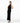 A female model wearing a sleek, black, ribbed yvy dress, standing in a minimalist white space. She is wearing pointed black heels