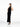A female model wearing a sleek, black, ribbed yvy dress, standing in a minimalist white space. She is wearing pointed black heels