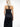 Back view of a female model wearing a black strapless tube dress paired with a black leather harness featuring crisscross straps and buckle details.